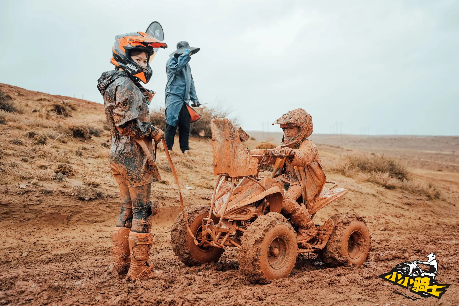 A young rider and an adult work through an ATV problem on a muddy route