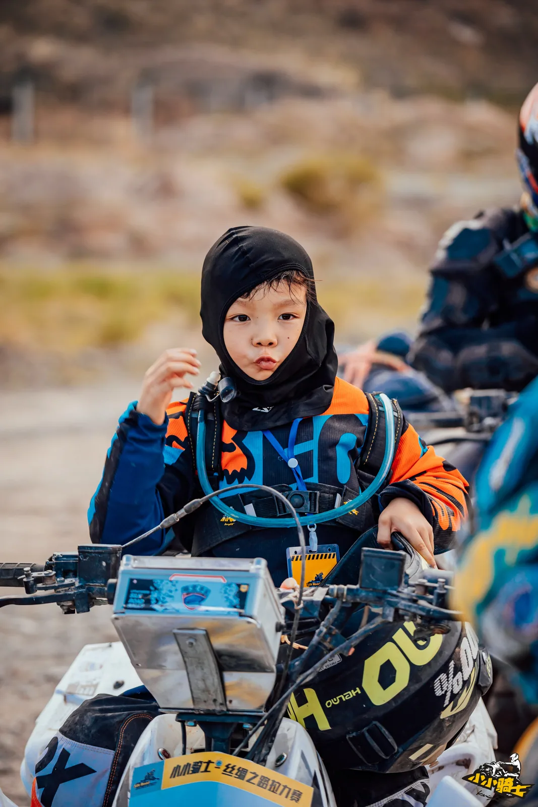 A young rider takes a quiet break beside an ATV and adjusts hydration gear