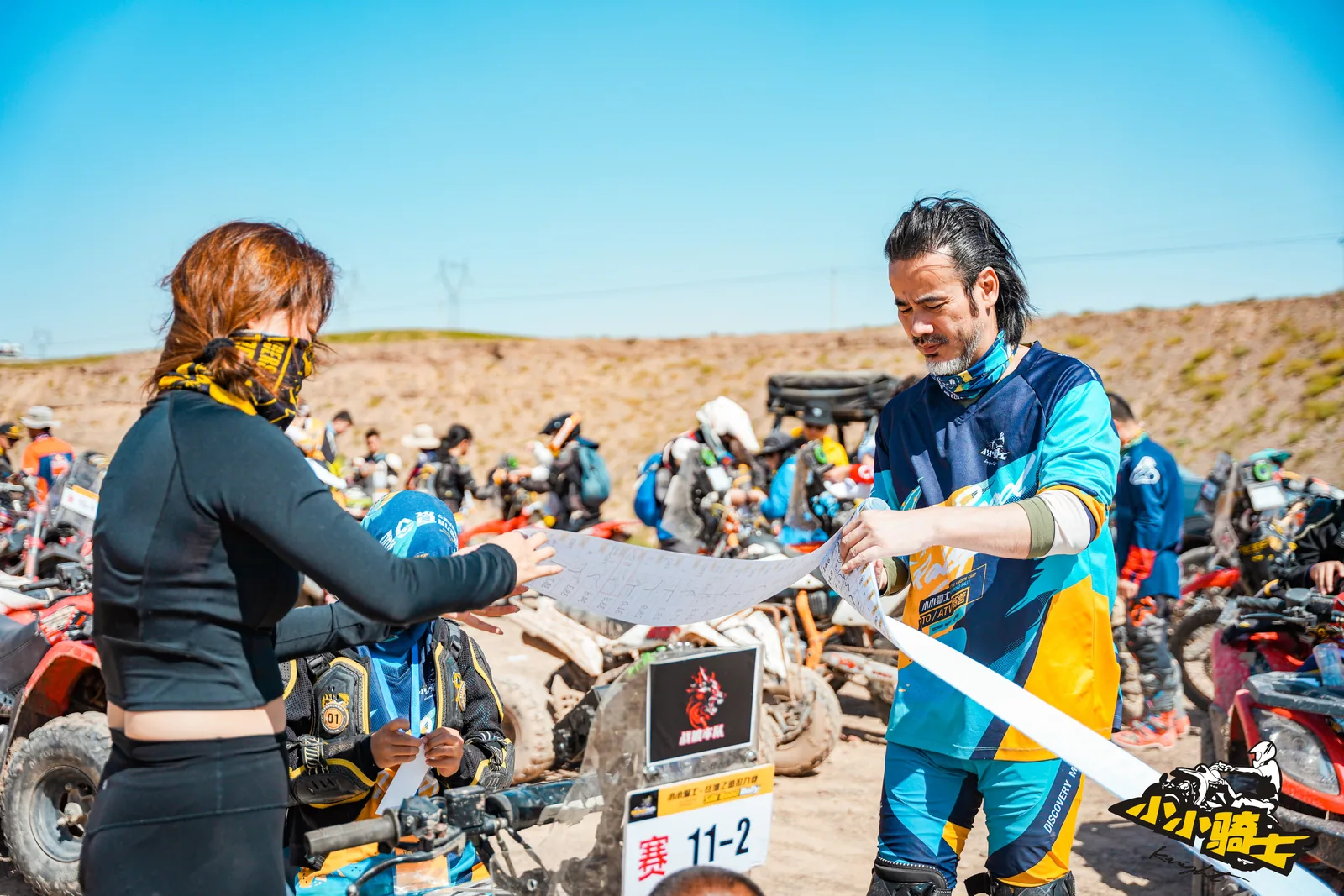 A coach and participants review and distribute rally roadbooks at the start area