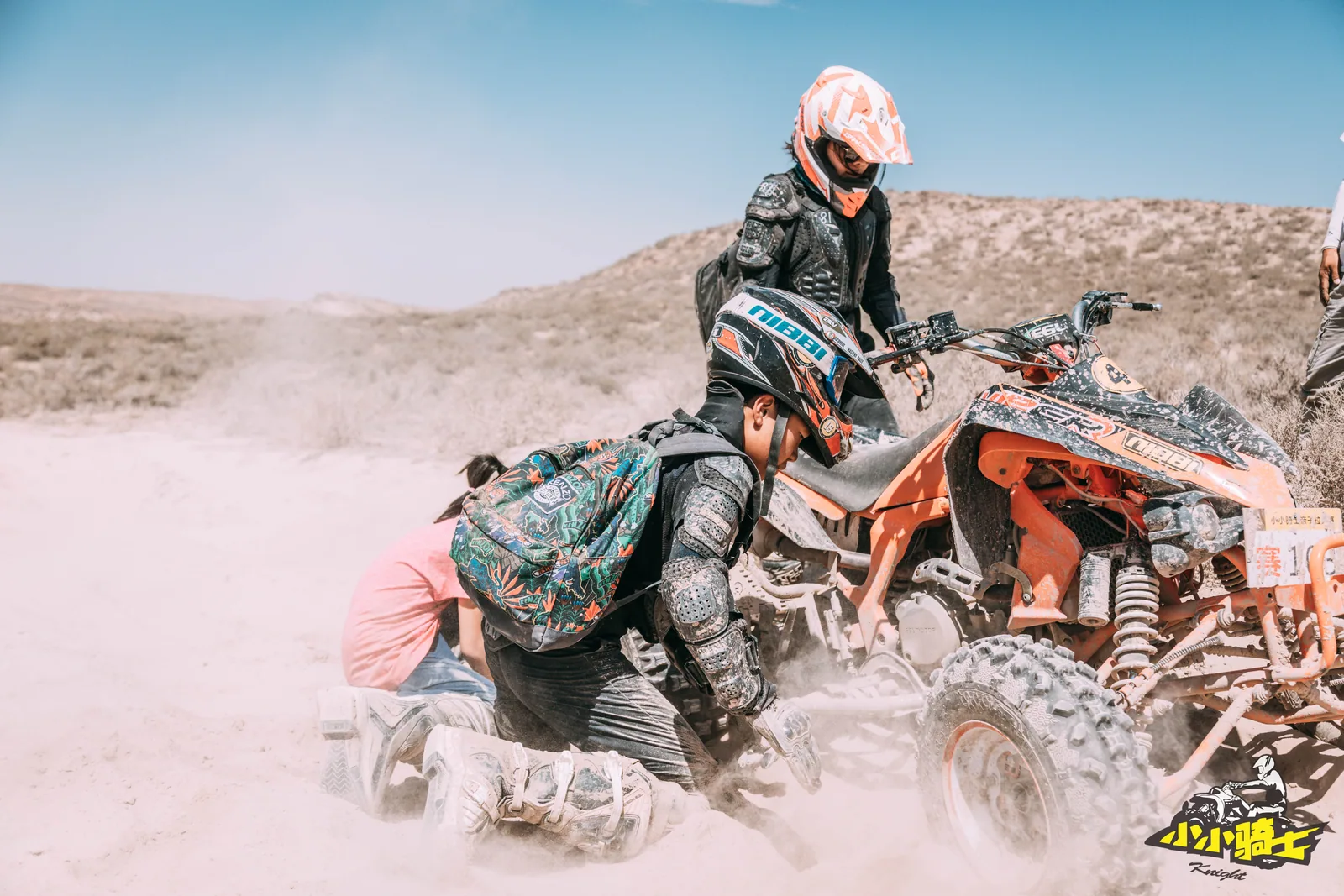 Participants and an adult kneel beside an ATV to inspect a mechanical problem
